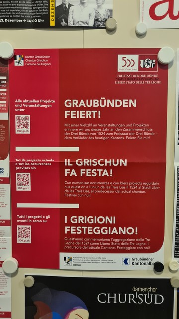 Ein rotes Plakat mit der Aufschrift Graubünden feiert in 3 Sprachen. 