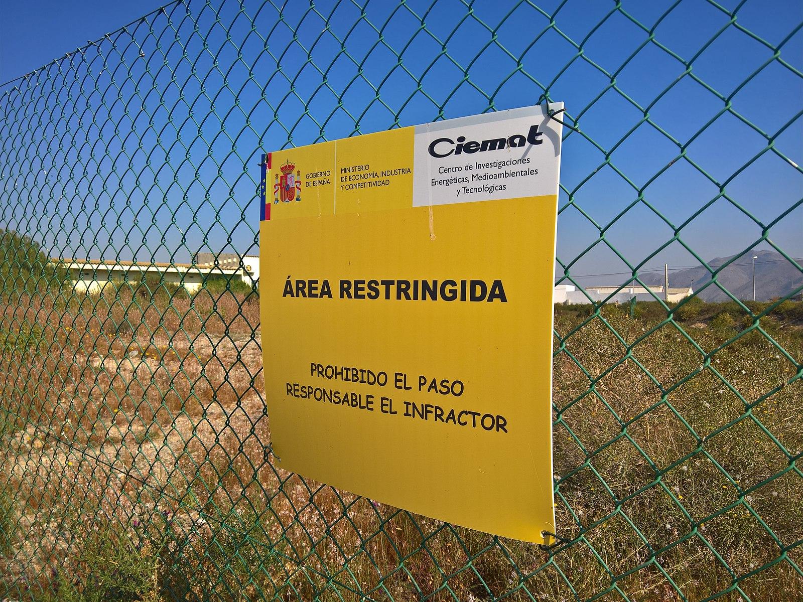 Foto: Gelbes Warnschild an einem Maschendrahtzaun. Neben Hoheitszeichen, sind Teile des Schildes mit Comic Sans beschriftet.

Cartel informativo de la zona de exclusión 1 de Palomares