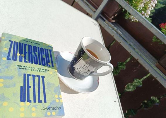 Buch: Zuversicht Jetzt und ein Becher mit Kaffee steht auf einem Tisch