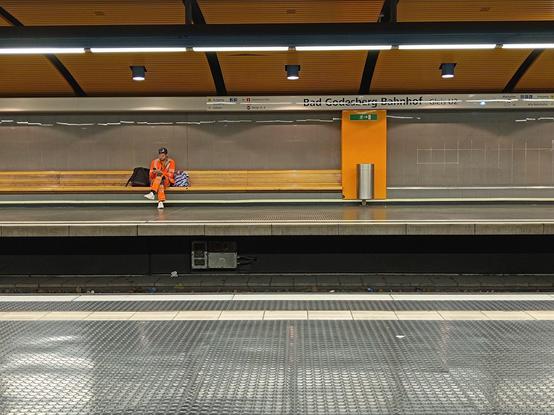 Mann sitzt in seiner orangenen Arbeitermontur allein auf einer Bank und wartet auf die U-Bahn.
