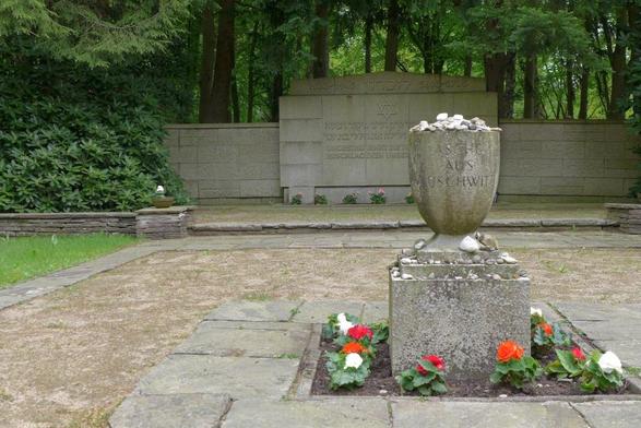 Gedenkstein Ohlsdorfer Friedhof. Aufschrift: Asche aus Ausschwitz. Umsäumt mit roten und weissen Blumen