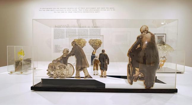 Hinter Plexiglas befinden sich Figuren aus geformeten Kunststoff wie alte Menschen im Rollstuhl, Kinder.