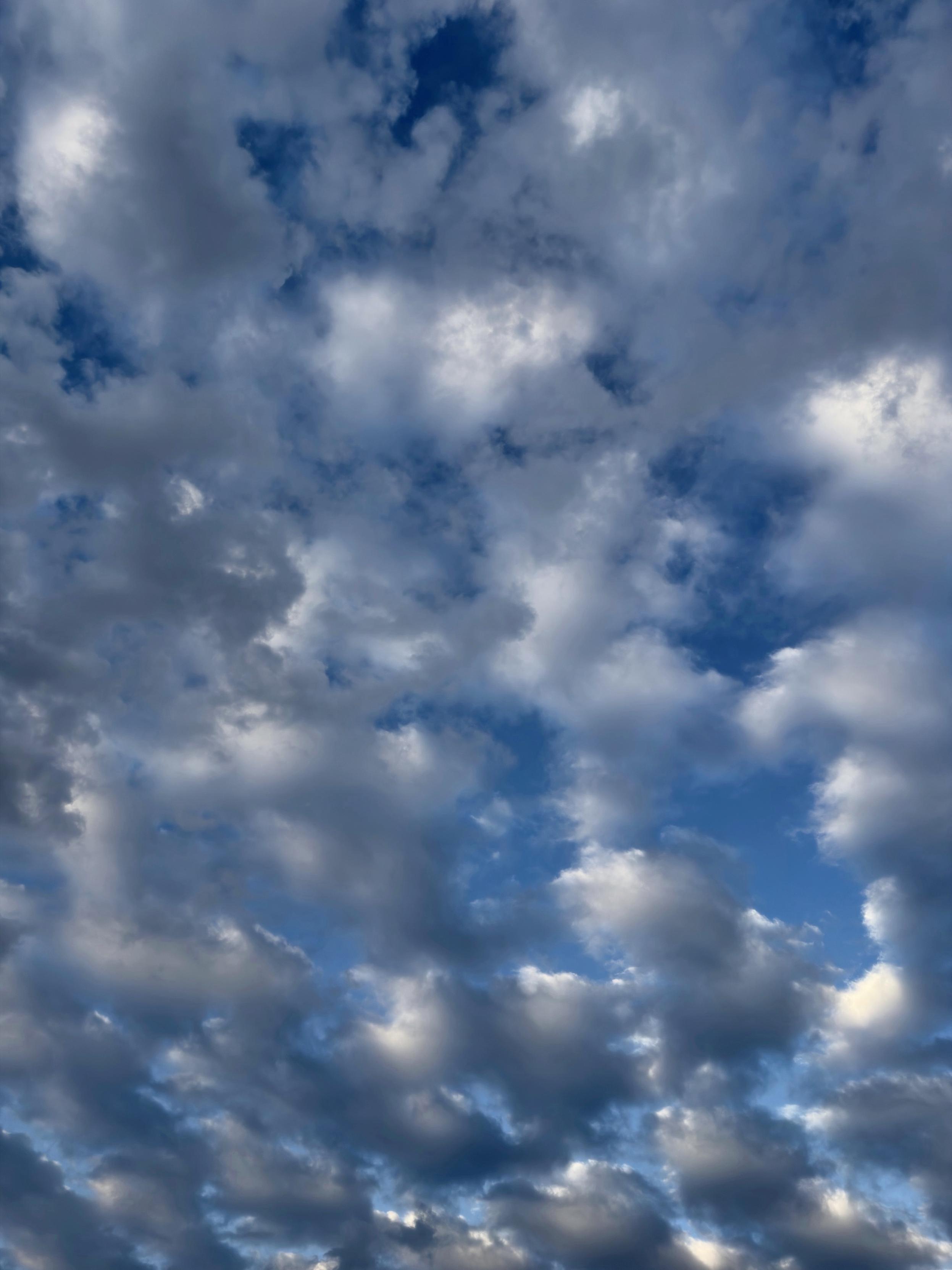Ein dynamischer Himmel voller wechselnder Wolkentöne, durchsetzt mit blauen Flecken. Die Wolken sind flauschig und geschichtet und erzeugen ein strukturiertes Aussehen.