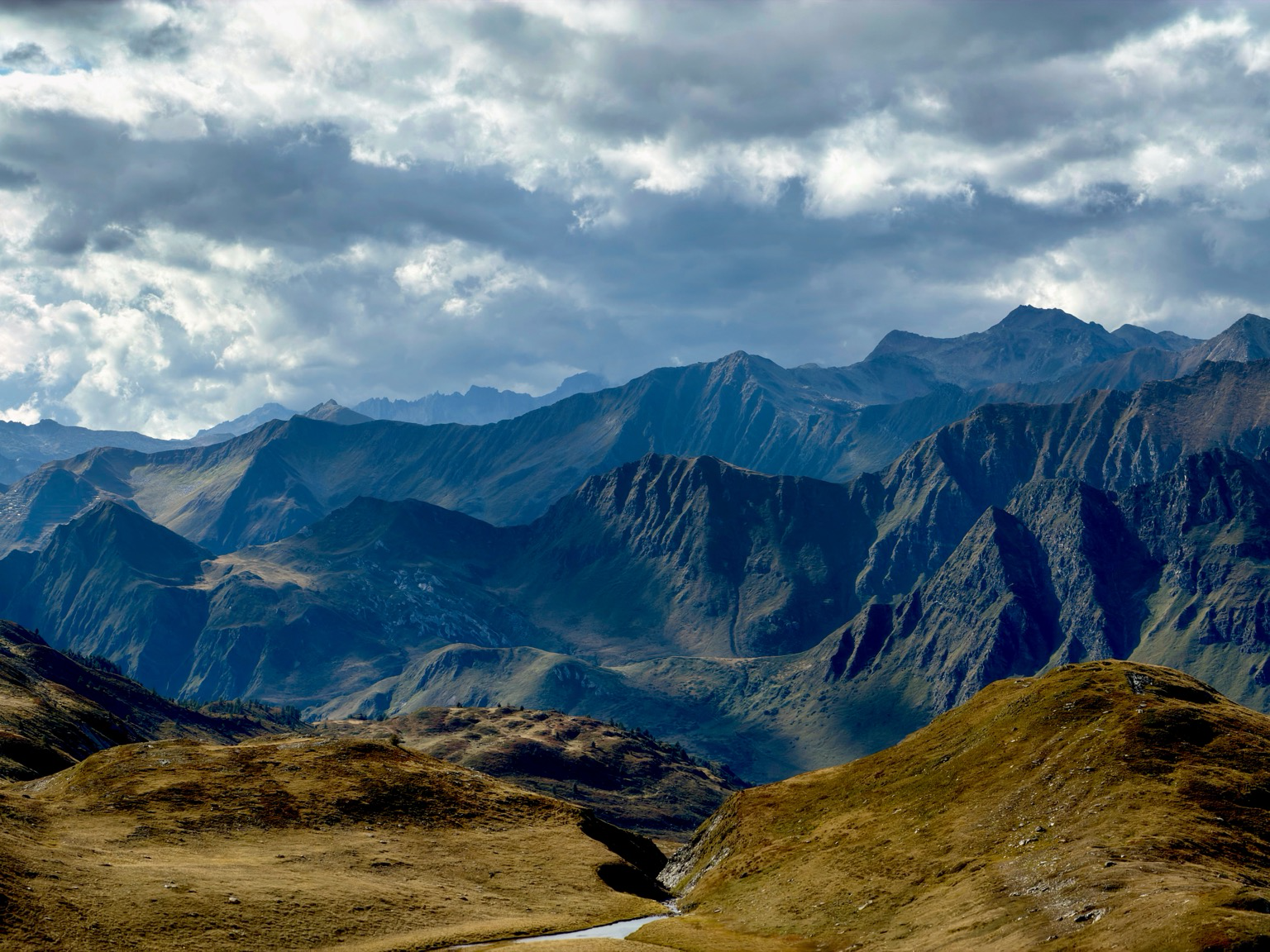 bergketten reihen sich an bergketten. vorne sind braune wiesen, der  himmel ist bewölkt