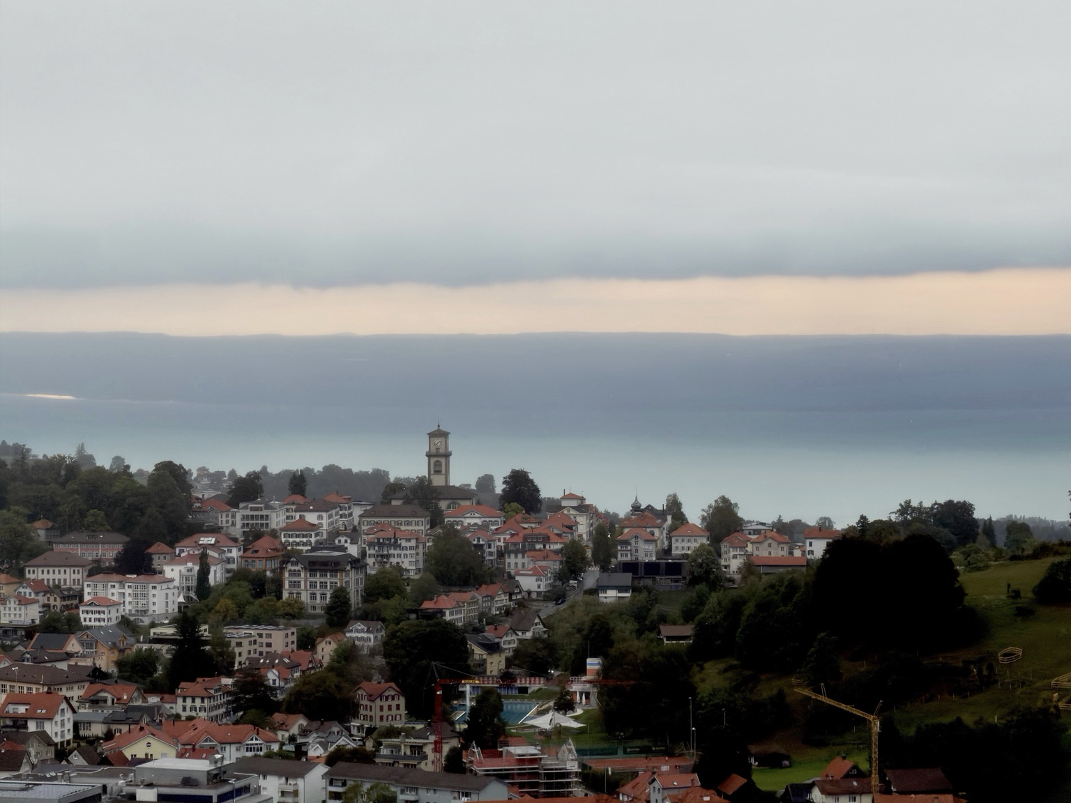 das dorf auf dem hügel. dahinter diffus der see und darüber ein wolkenband