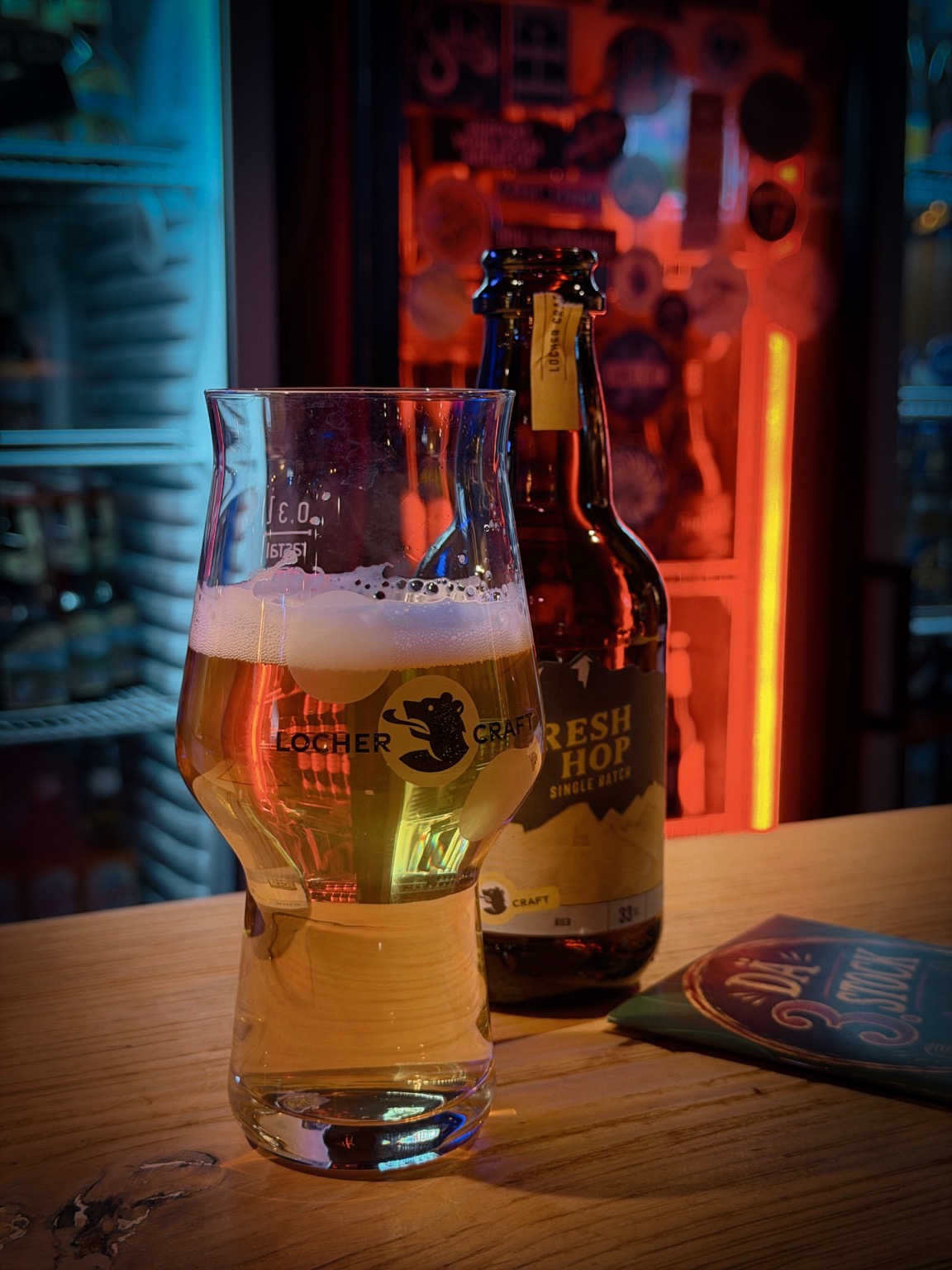 ein bierglas vor einer bierflasche vor einem bierkühlschrank