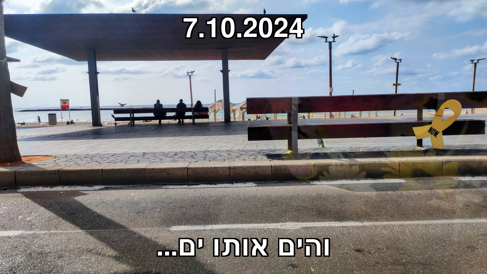 צילום של חוף בוגרשוב בתל אביב (שנה אחרי 7.10.2023): קרוב אלינו יש ספסל ועליו שלט NOW בצורת סרט צהוב. במרחק יש 3 דמויות שמביטות לשקיעה.
כיתוב בסגנון מים:
7.10.2024
והים אותו ים...