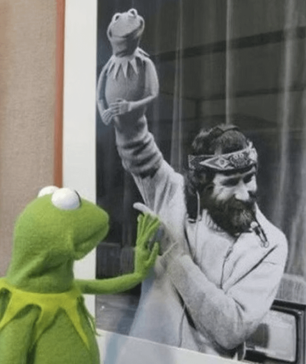 A poignant image of Kermit the Frog looking at a black-and-white photograph and touching the hand of his late creator, Jim Henson.