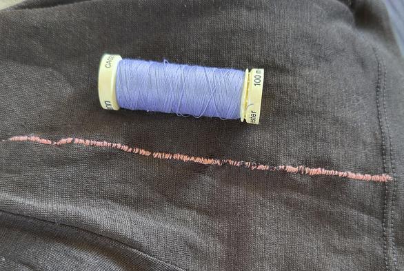 a long line of peach-coloured stitching in a black merino base layer. a bobbin of   lavender-blue coloured gütermann thread is shown for scale. because it's a really, really long line of stitching. like, really long. repairing what amount to runs/ladders in merino is not fun. and takes ages. did i mention it's a really long line of stitching?