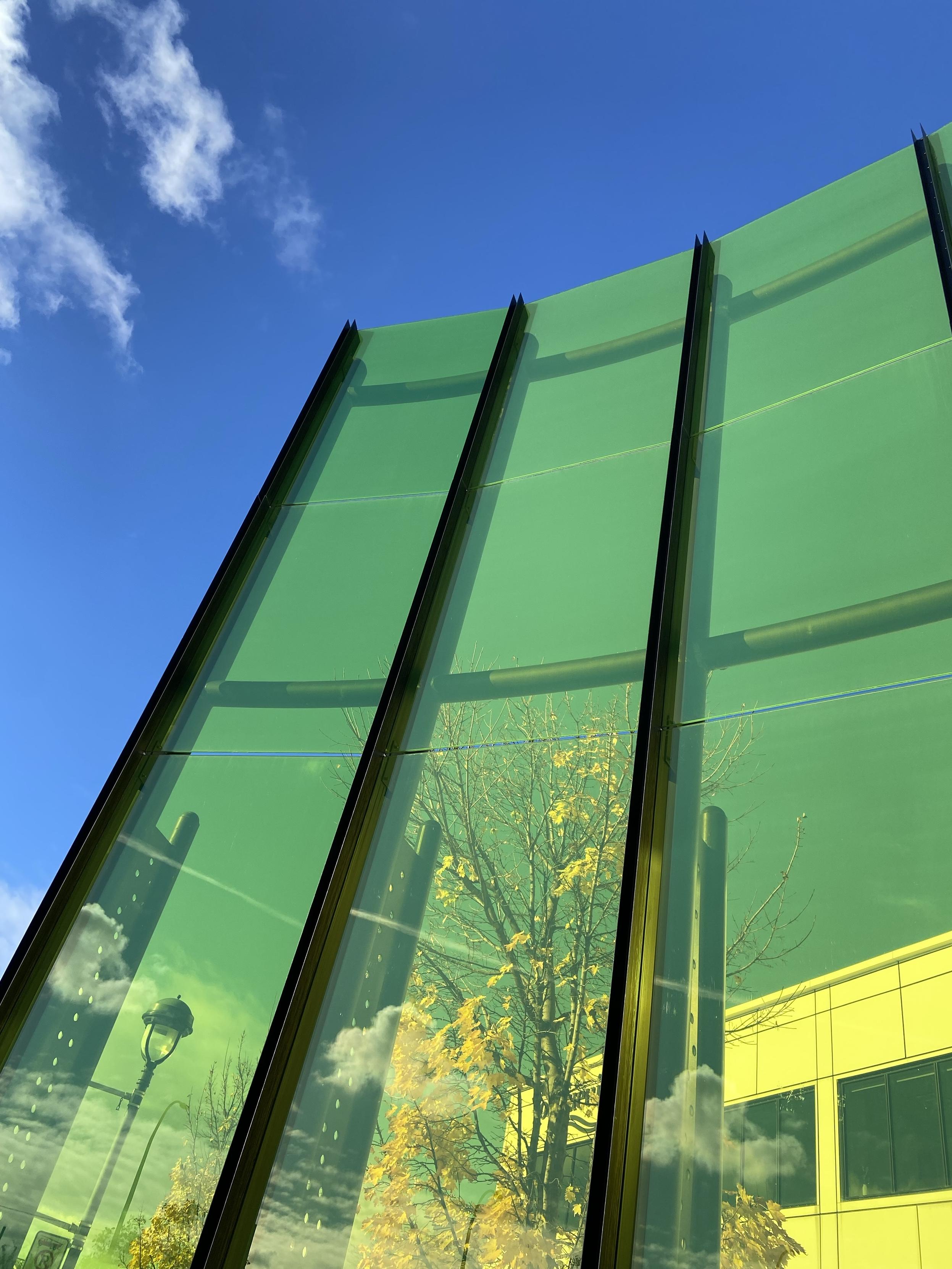A tall structure/wall of yellow glass, but it looks green because the sky behind is blue. To the left and top, we also see the blue sky directly, without the glass in between. 