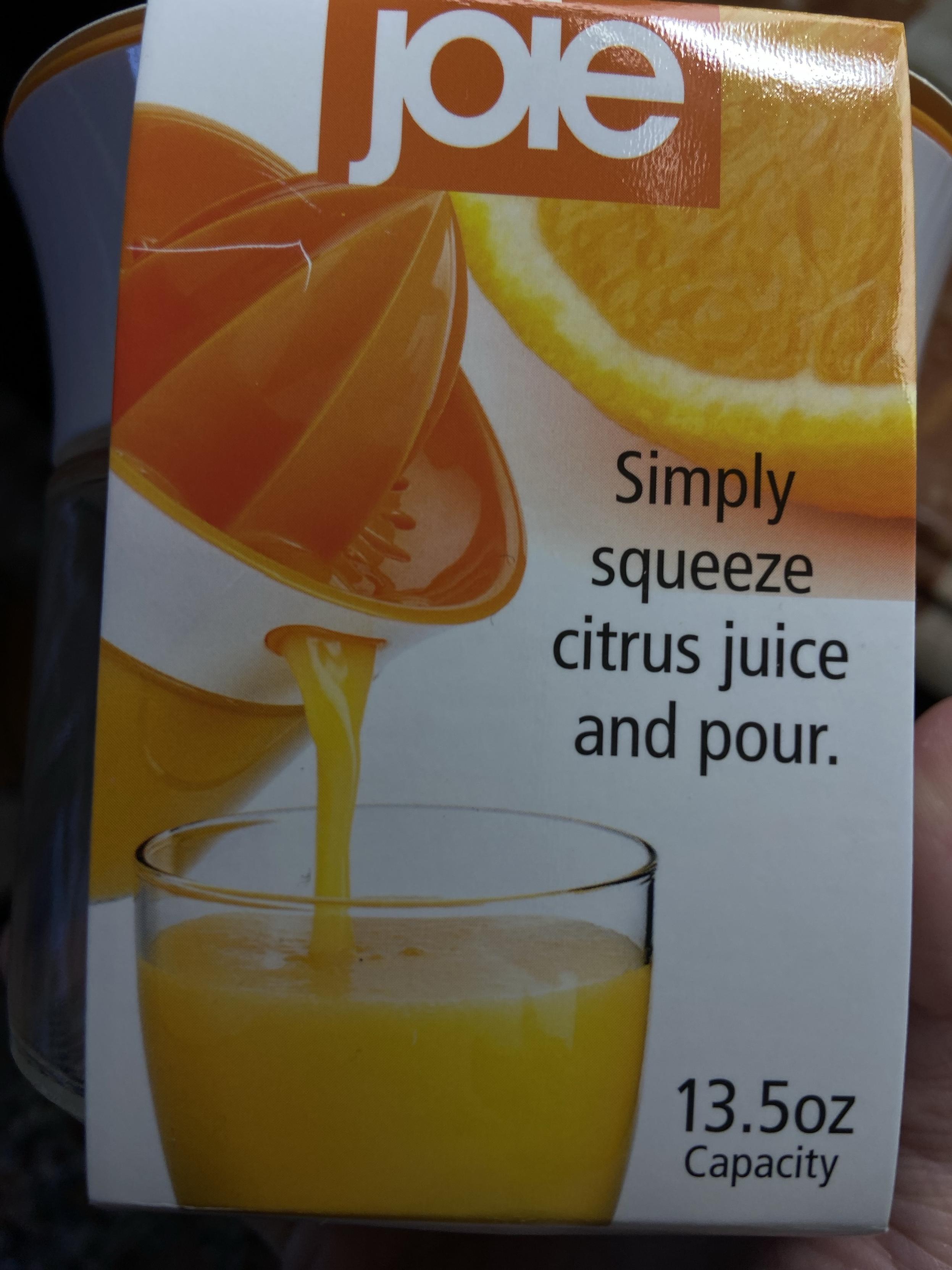 Under the brand name Joie, the text reads "Simply squeeze citrus juice and pour." There's an orange slice in the background, and in the foreground there's a citrus juicer with an orange reamer on top of a glass jar, and it's being tilted to pour juice out of a little opening in the side, and frankly it looks like a witch with an orange hat is barfing.