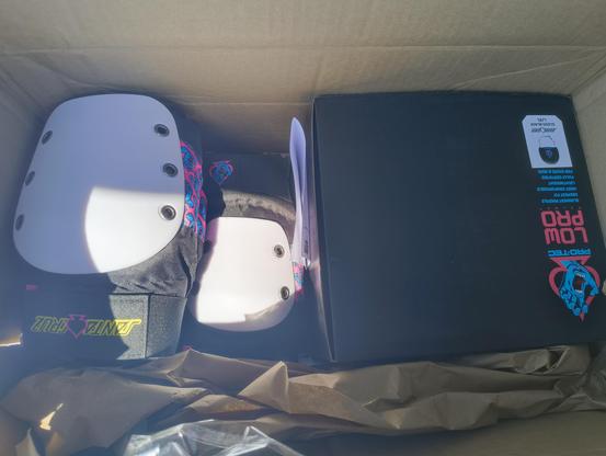 Shipment box with Pro-tec skate gear. You can see some kneepads and a black box with a helmet in there. Both have the iconic blue, pink, and white trans colours.