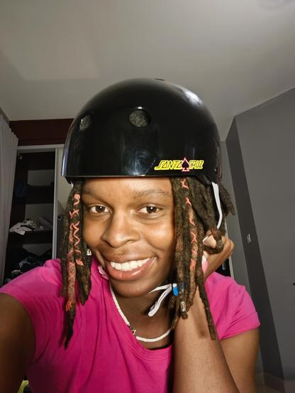 Cute selfie of a black trans girl with locs smiling with a black Santa Cruz pro-tec helmet.