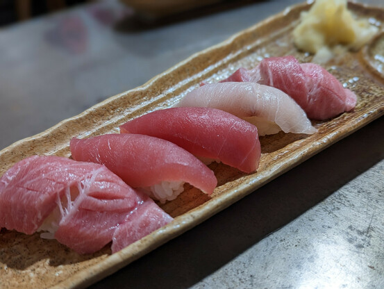 5 pieces of nigirizushi on a brown rectangular dish. Sushi includes o-toro, maguro, and another white fish.