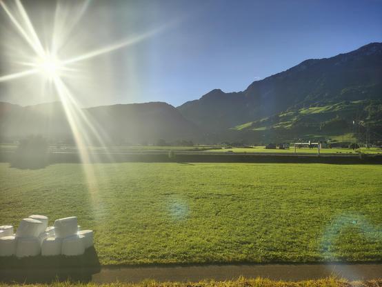 A photo of the sun rising behind mountain taken from a train with a Swiss farm in the foreground.