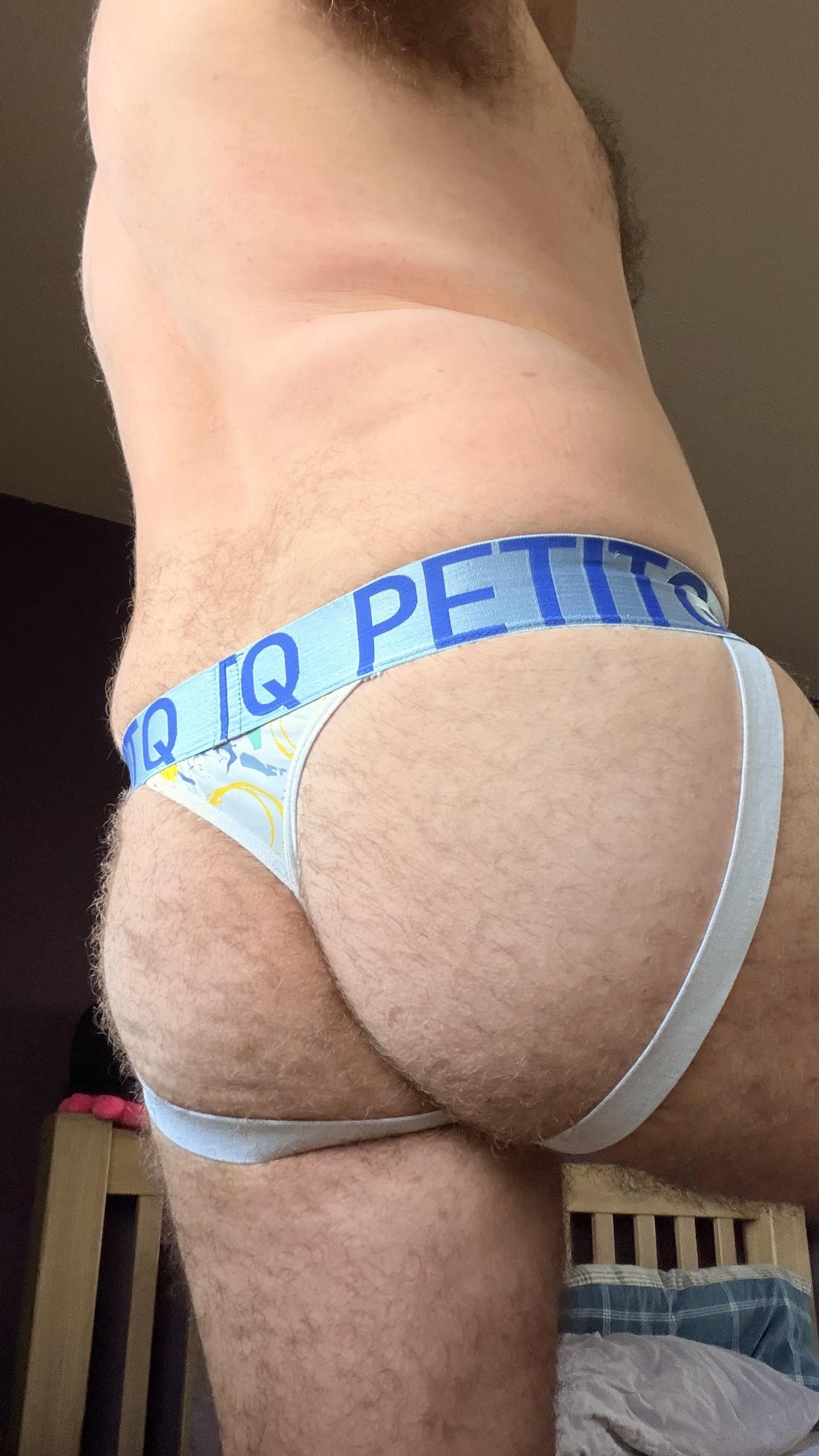 Hairy gay guy showing off his arse in a white Petit-Q jockstrap thong with blue, green, and yellow circle pattern
