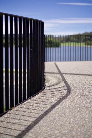 Photograph of curved shadows made by a metal fence and railing on a concrete path.