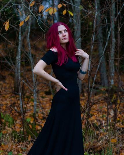 A witchy red haired woman standing in a cold autumn forest in a long black dress