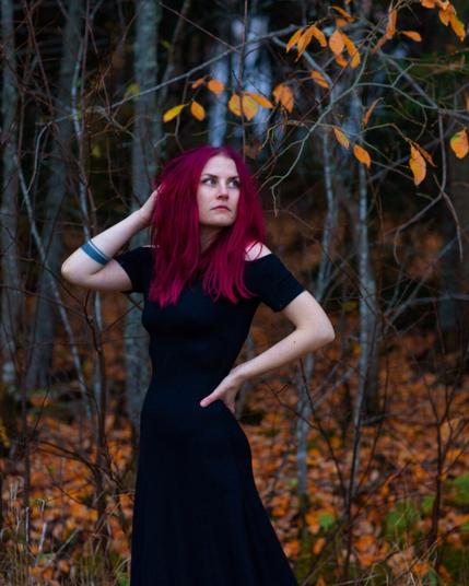 A witchy red haired woman standing in a cold autumn forest in a long black dress