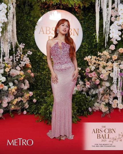A ginger-haired lady wearing a pinkish dress, posing for a photo.