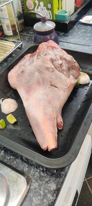 A large leg of lamb in a roasting tray, accompanied by a halved garlic head and some segments of lime. There's a sprig of rosemary underneath, but you can't see it in the photograph.