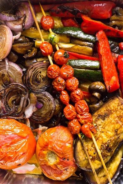 Assorted balsamic-grilled vegetables including skewered cherry tomatoes, sliced zucchini, red bell peppers, eggplant, red onions, mushrooms, and whole roasted tomatoes, all glistening with marinade and charred to perfection.