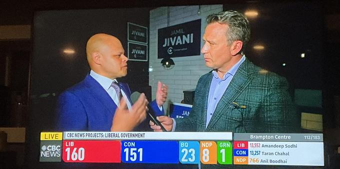 Two men on screen, a man in a blue suit is gesturing.