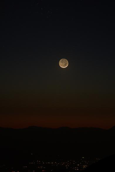 The moon, only a few degrees above the horizon, now has an obvious yellow tint. The lights of La Luz village are at the bottom of the frame.
