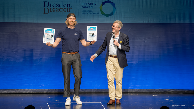 Foto von Marco Gustav, der auf einer Bühne zwei Preise in den Händen hält. Neben ihm steht Prof. Gianaurelio Cuniberti, Professor für Materialwissenschaft und Nanotechnik an der TU Dresden.