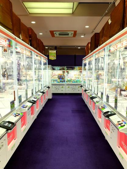 An aisle in the arcade lined with grappler machines. The carpet is purple, the walls are dark red, and everything else is bright and shiny. Magically, I managed to take this shot while nobody was in this area.