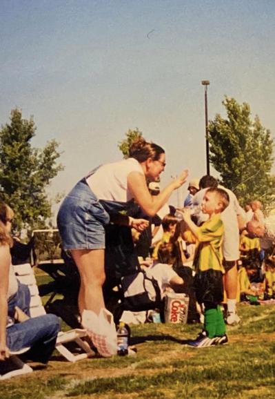 This is an image of a mom leaning forward to give advice to her young son (about 4 years old) on the sidelines of his youth soccer game. He's looking at her and listening while drinking from a bottle of water.