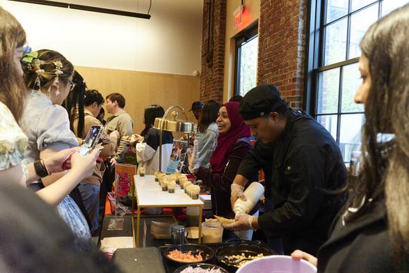 A crowd of attendees surrounding a table at a food market event.