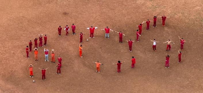 Aerial footage of a dirt field with people dressed in red outfits spelling out S O S
From a detention center in texas which is which is deporting people to el salvadorian gulags