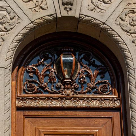 A close-up of the woodwork above the door. Wooden curls and flowers frame a lamp of glass set in wood.