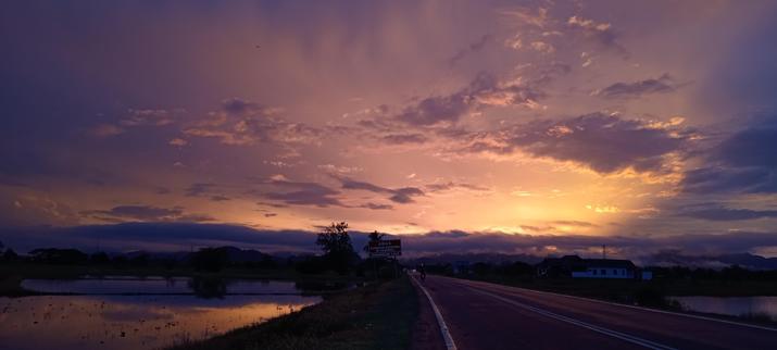 Orange and purple sunset over the Perlis landscape bisected by the road with water-filled, to-be-planted rice fields reflecting the sky on both sides.
