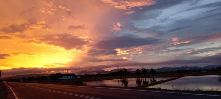 Orange sky on the left meets the blue on the right during a sunset over the Perlis landscape. Water-filled, to-be-planted rice fields reflect the blue side of the sky.