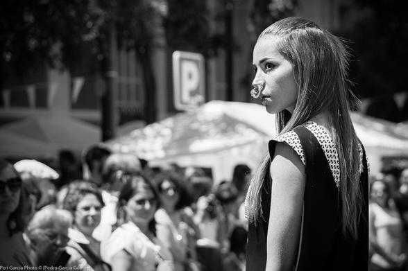 Foto en blanco y negro y plano medio y de perfil de una de las modelos mirando a la izquierda con el fondo desenfocado del público, carpas del festival y los edificios del fondo. Destaca que la modelo lleva un gran aro en la nariz.