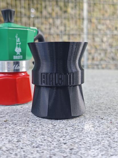 The stand and funnel extension 3d-printed in black filament, assembled. There's a green and red La Mokina in the background.