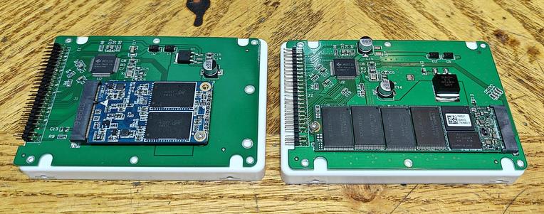 The image shows two printed circuit boards (PCBs) mounted in white plastic casings, likely representing solid-state drives (SSDs). They are placed side-by-side on a wooden surface.

On the **left**, the PCB has a single, smaller blue M.2 SSD card inserted into a slot. There are also several other electronic components visible on the green PCB.

On the **right**, the PCB has four black NAND flash memory chips on a longer green PCB. There's also a smaller component that could be a controller chip.

Both PCBs have IDE connectors on the left side for interfacing with a system.