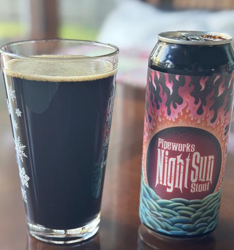 Full glass of Pipeworks Night Sun Stout right next to the can, showing the fiery logo design