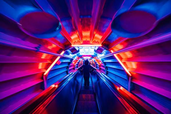 A kid is going down a dark elevator illumitated with colourful light effects at the Atomium in Brussels. Only his silhouette is visible on a blue and red background.