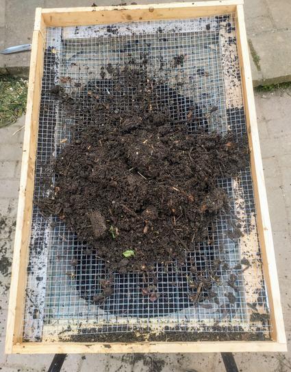 A photo of the same contraption, with a half-inch silver mesh inserted into the frame. A pile of unsieved homemade compost has been heaped on the frame.

No chickens are visible, sadly.