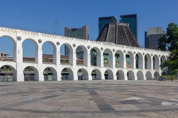 The image features an architectural structure known for its white arches, surrounded by modern buildings in the background. This scene depicts a blend of historical and contemporary elements, likely showcasing urban architecture. The structure appears to be a prominent landmark, possibly an aqueduct or a similar feature, with a clear blue sky overhead. The area surrounding it seems to be paved, adding to the urban aesthetic.

Image Credits: Wikimedia / Photograph by Mike Peel (www.mikepeel.net). / CC BY-SA 4.0