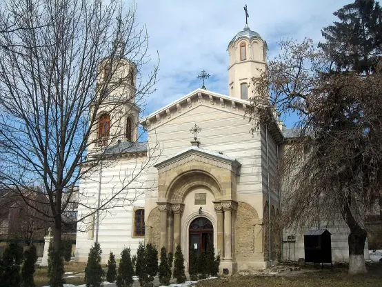 The image appears to depict a church, showcasing a blend of architectural styles. It features two towers and a prominent entrance with decorative elements. The building is set amidst trees, with some branches visible in the foreground, suggesting a serene outdoor setting. The architecture may include domes and crosses, common in many Eastern Orthodox churches.

Image Credits: Wikimedia / Cezar Suceveanu / CC BY 3.0