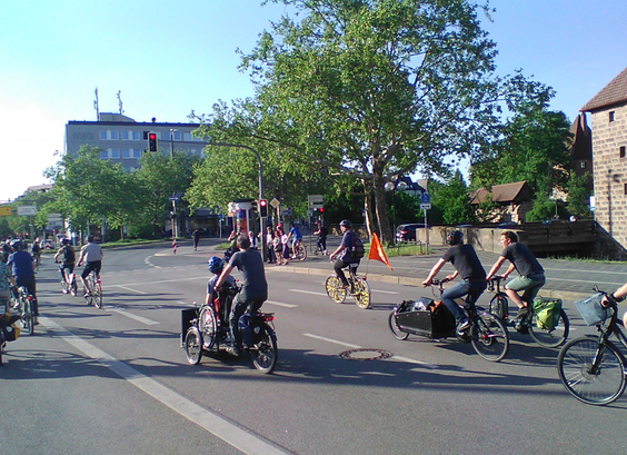 Radfahrende der Raddemo fahren auf dem Altstadtring Richtung Plärrer, rechts zu sehen sind Teile der alten Stadtmauer, ein Rad hat mit XR-Zeichen im Vorderrad und auf orangener Fahne, im Vordergrund ein Lastenrad mit Rollstuhlfahrer im Fond