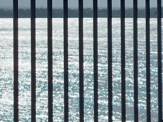 .. a "grill" of metal bars fill the entire frame of the capture .. 11 in total .. spread evenly several inches apart .. a south facing view & a sea vista glistens in the evening sunlight beyond ..