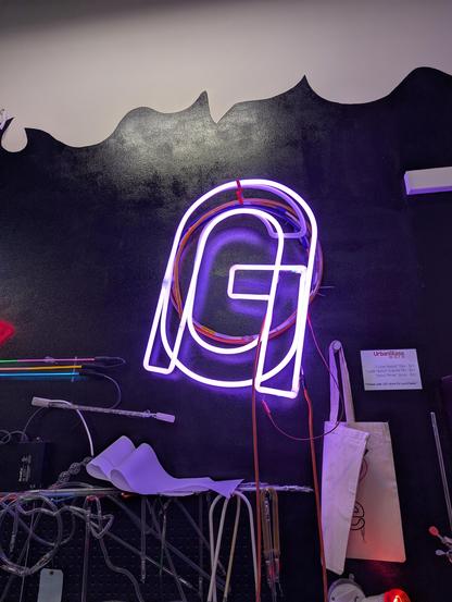 Big pink "G" with upside down "U" in front of it hung on a black wall, turned on from the orange wires of the aging transformer while the mercury vaporizes through the rest of the G and makes the top of it bright