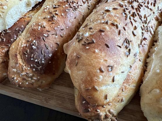 Auf einem dunklen Holztisch liegt ein Holzbrett. Darauf liegen zahlreiche frisch gebackene Brötchen mit rustikalem Ausbund.