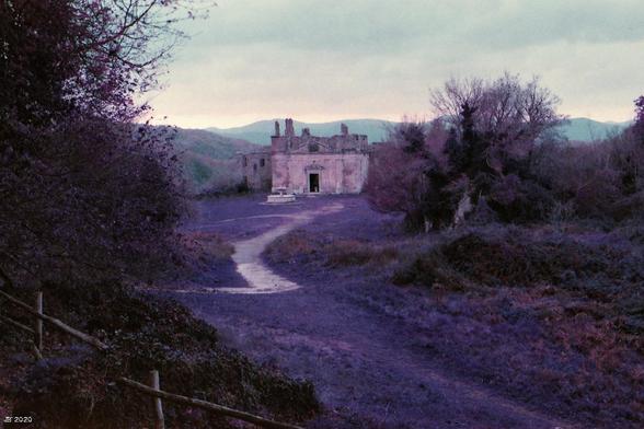 Ein verwunschener Blick auf einen Teil der Geisterstadt Antica Monterano in Lazio, Italien. In Bildmitte die Ruine der Kirche. Verfremdete Farben in violett, rosa und braun durch den verwendeten Purple-Film. Leica R4 mit 50 mm Summilux.