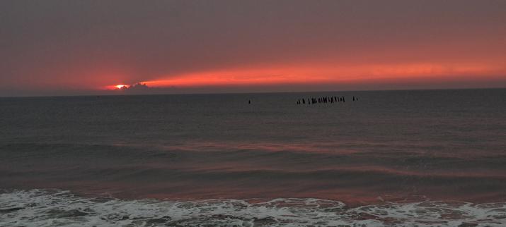 Happy Monday to all of us. Yes there's a thing like that. Sun rising behind the clouds at the Promenade. Sea is tranquil and sky is grayish orange.
